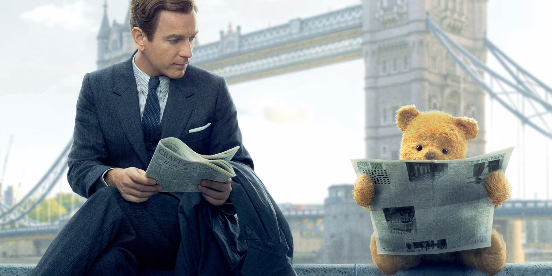 Christopher Robin, as an adult, holding a newspaper, as Winnie the Pooh holds one reading (upside-down) beside him, with the London Bridge behind them.
